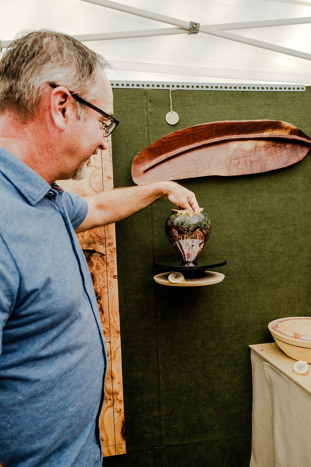 A visitor admiring hand-turned wood art in a vendor tent